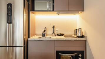 Eine kompakte Küche mit Edelstahl-Kühlschrank, Mikrowelle, Backofen und Kaffeemaschine.