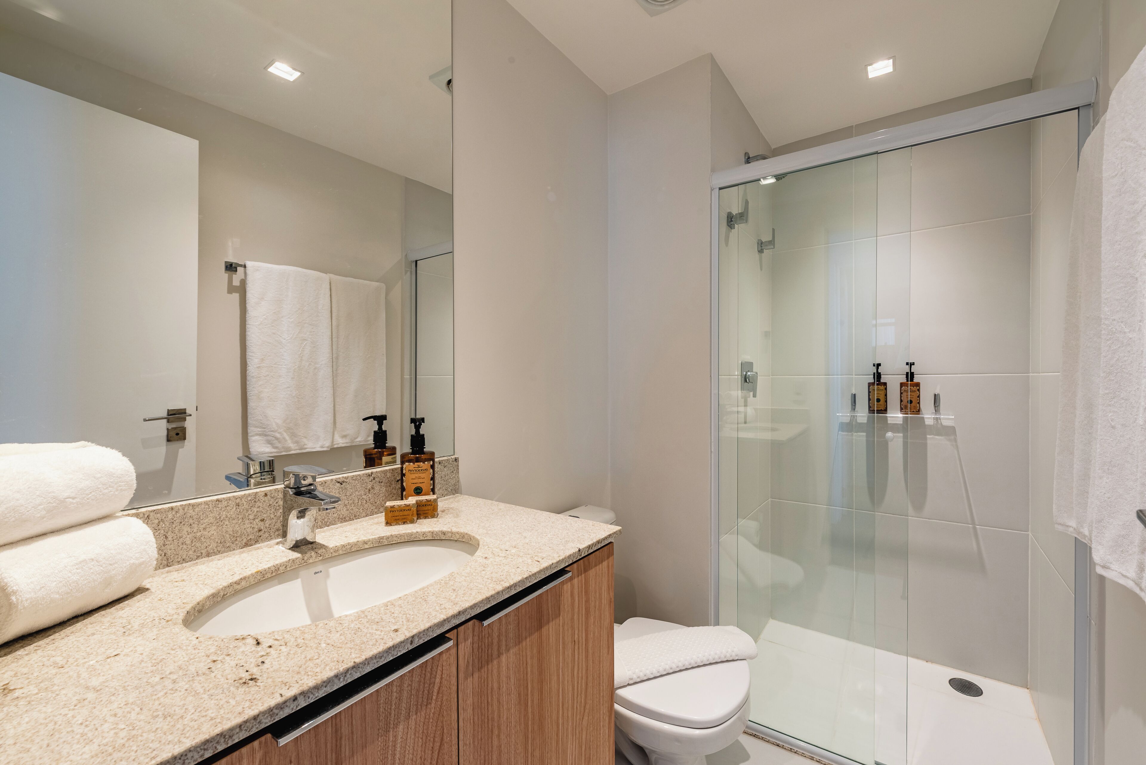 A modern bathroom with a granite countertop, a white sink, a glass-enclosed shower, and a large mirror.