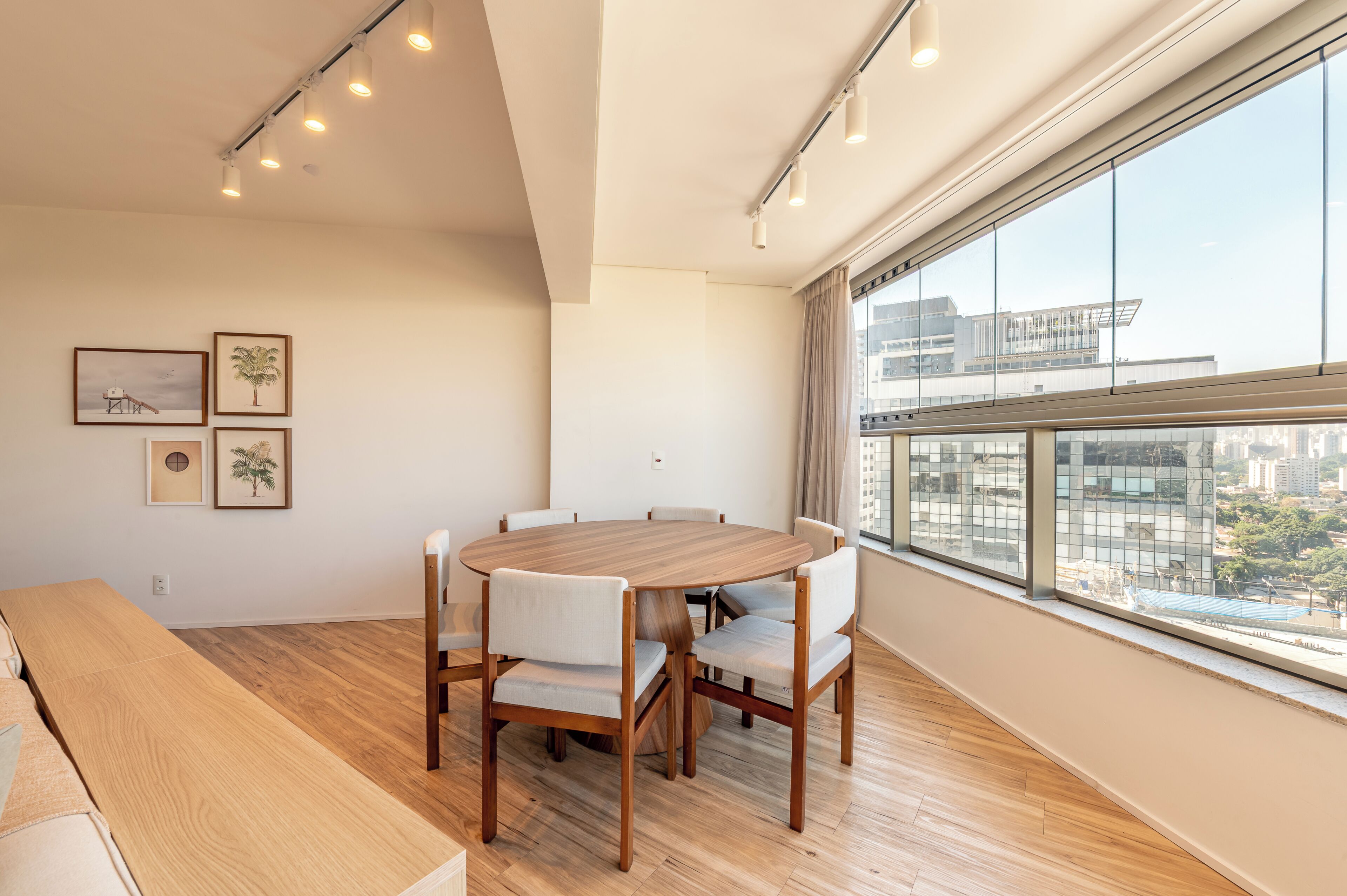 Ein moderner Essbereich mit einem runden Tisch und Stühlen, großen Fenstern mit Blick auf die Stadt und gerahmten Kunstwerken an der Wand.