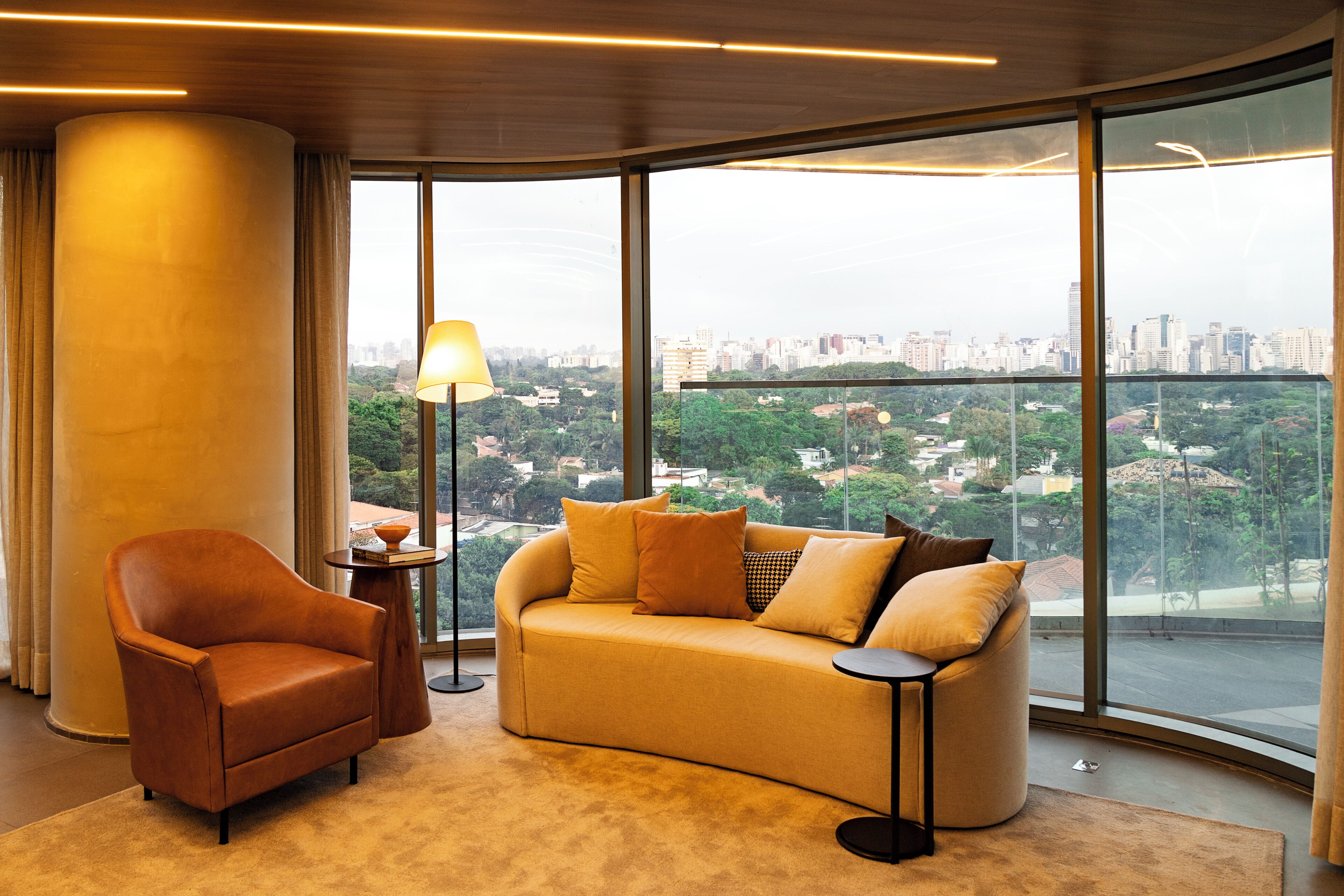 A modern living room with a sofa, armchair, and floor lamp, large windows with a city view.