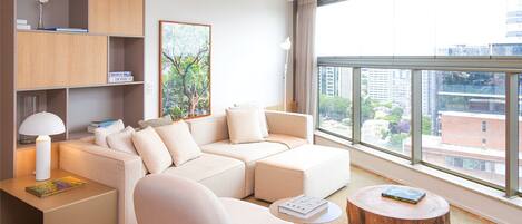 Una sala de estar moderna con un sofá seccional, una mesa redonda para café, una mesita de noche con una lámpara y un ventanal con vistas a la ciudad.