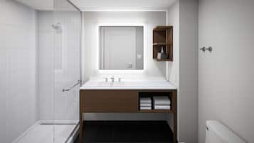 Un baño moderno con cabina de ducha de vidrio, un lavamanos blanco y un mueble de tocador de madera, y un inodoro.