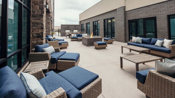 Un patio al aire libre con mobiliario de mimbre, un hogar para fogata y vistas del exterior del edificio.