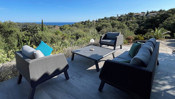 A deck with outdoor furniture, including a sofa and chairs, overlooking a scenic landscape with trees and a distant view of the sea. - Villa "terre D'azur" Avec vue mer , Piscine, Jardin Clos, Rénovée (La Croix-Valmer)