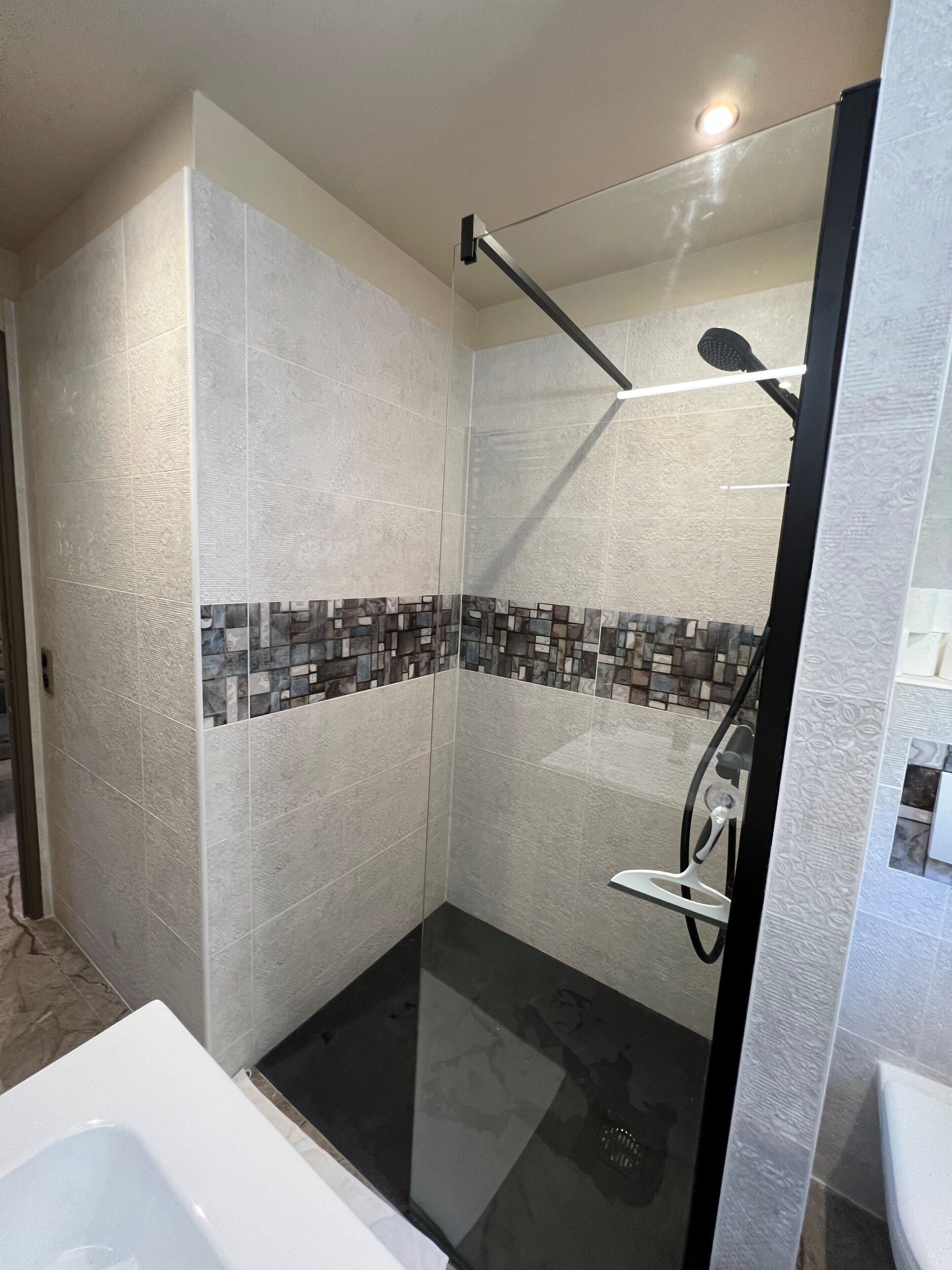 A modern shower area with a glass door, a handheld showerhead, and a tiled wall with a mosaic pattern.