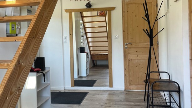 Un intérieur moderne avec un escalier en bois, une pancarte « Bienvenue », un espace de couchage en mezzanine et un présentoir en métal noir.