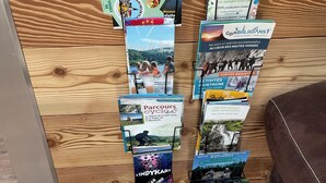 Un présentoir avec des brochures de voyage et des cartes, fixé à un mur en bois, devant lequel se trouve une petite table.