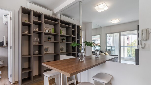 Een moderne keuken met een houten aanrecht, witte krukken en een ingebouwde open kast met decoratieve objecten.
