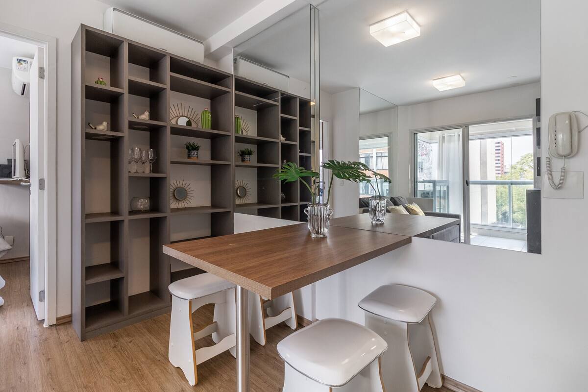 A modern kitchen with a wooden countertop, white stools, and a built-in shelving unit with decorative items.