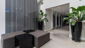 Een moderne lobby met een zithoek, een grote potplant en een reflecterende plafondlamp.