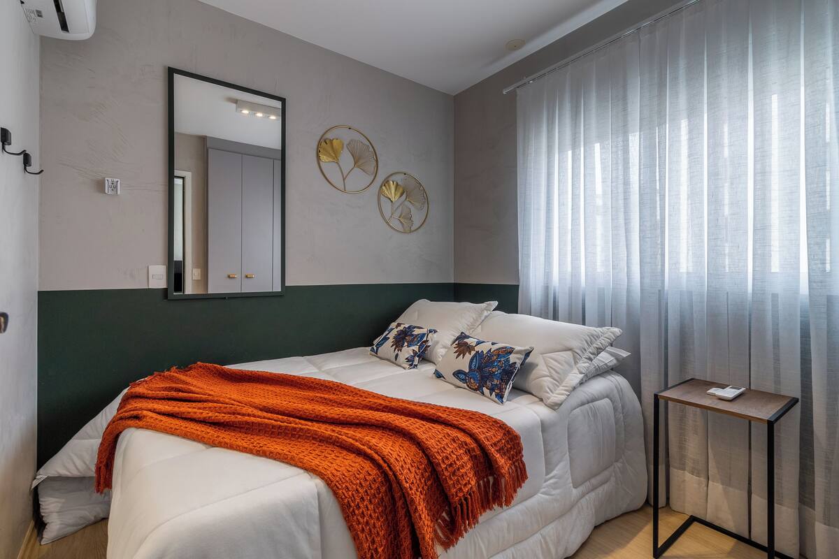 A neatly arranged bedroom with a bed, a bedside table, a mirror, and two wall decorations.