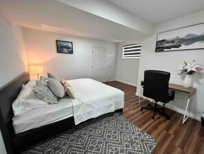 Une chambre à coucher avec un lit, un bureau, une chaise, une lampe et un tableau au mur.