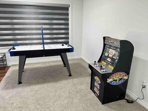 Une table de baby-foot et une console de jeux vidéo se trouvent dans une pièce dont le sol est recouvert d’une moquette et qui possède une fenêtre avec des stores.
