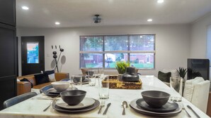 A modern dining area with a marble table set for four, a large window with blinds, and a view of a residential area.