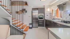 Una cocina moderna con horno empotrado, refrigerador de acero inoxidable y un amplio ventanal con cortinas.