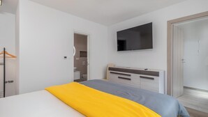 Un dormitorio con una cama, un televisor montado en la pared y un baño visible a través de una puerta abierta.
