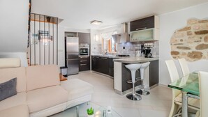 Una cocina moderna con una isla central, electrodomésticos integrados y un comedor con mesa de vidrio y sillas blancas.