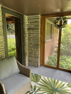 A corner room with a wicker sofa, a glass door, a brick wall, and a view of greenery. - Chucle Homestead - Charming 3 bdrm, 2 bath ranch home (Maryland)