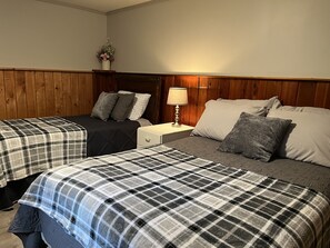 Una habitación de hotel con dos camas, una mesita de noche con lámpara y cabecera de madera.