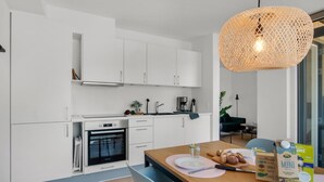 Een moderne keuken met witte kastjes, een inbouwoven en een eethoek met een houten tafel.