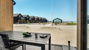 Een houten tafel met een fruitschaal en een mok, met uitzicht op een strand met moderne gebouwen en een heldere lucht.