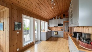A spacious kitchen with wooden walls and a high ceiling, featuring a large window, a built-in oven, and a coffee machine. - Beautiful home in Sjusjøen with sauna (Sjusjøen)