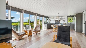 En moderne stue med et fjernsyn, læderstole, et træbord og et køkken i baggrunden.