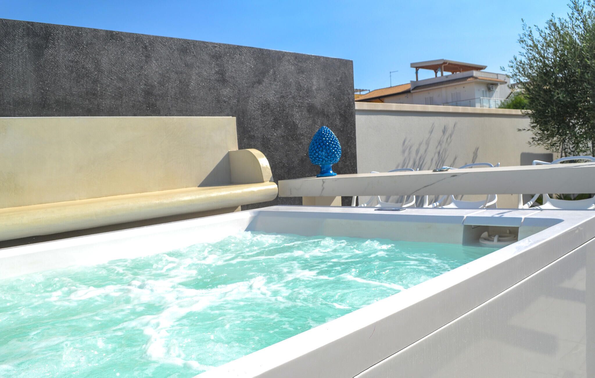 A modern outdoor pool area with a clear water feature, a textured wall, and a building in the background.