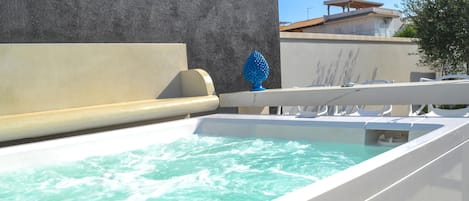 A modern outdoor pool area with a clear water feature, a textured wall, and a building in the background.