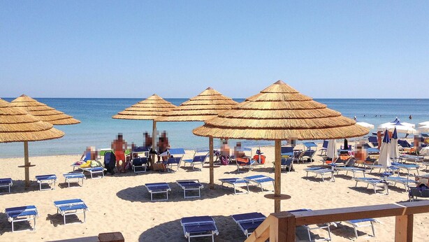 En strand med parasoller av halm och solstolar.