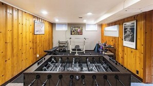 A room with wooden paneling, a foosball table, a bench, and a weightlifting area.