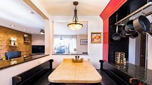 A modern kitchen with a central island, black leather seating, and a hanging pot rack.