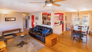 A spacious living room with a black leather sofa, a wooden coffee table, and a dining area with a wooden table and chairs.