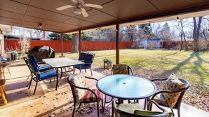 A covered patio area with a table and chairs, a ceiling fan, and a view of the backyard.