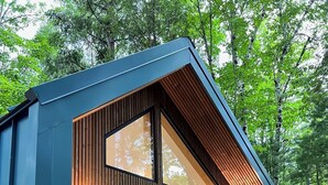Eine moderne Holzhütte mit großen Glasfenstern und einer Terrasse mit Sitzgelegenheiten.