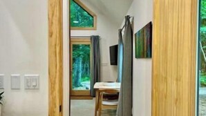 Ein Flur mit einer Holztür, einem Waschbecken und einem Fenster, das in einen Essbereich mit Tisch und Stühlen führt.