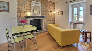 Une pièce avec un mur en pierre, une cheminée, un canapé jaune, une table à manger avec des chaises et une fenêtre donnant sur un beau paysage.