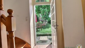 Un escalier en bois mène à une porte qui donne sur un jardin où se trouvent une chaise et une table.