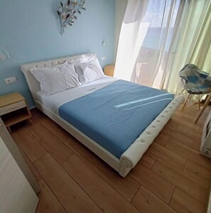 A bedroom with a bed, a nightstand, a chair, and a window with curtains.