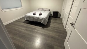 Ein Schlafzimmer mit einem Bett, einem Nachttisch, einem Fenster mit Jalousien und einer Tür.