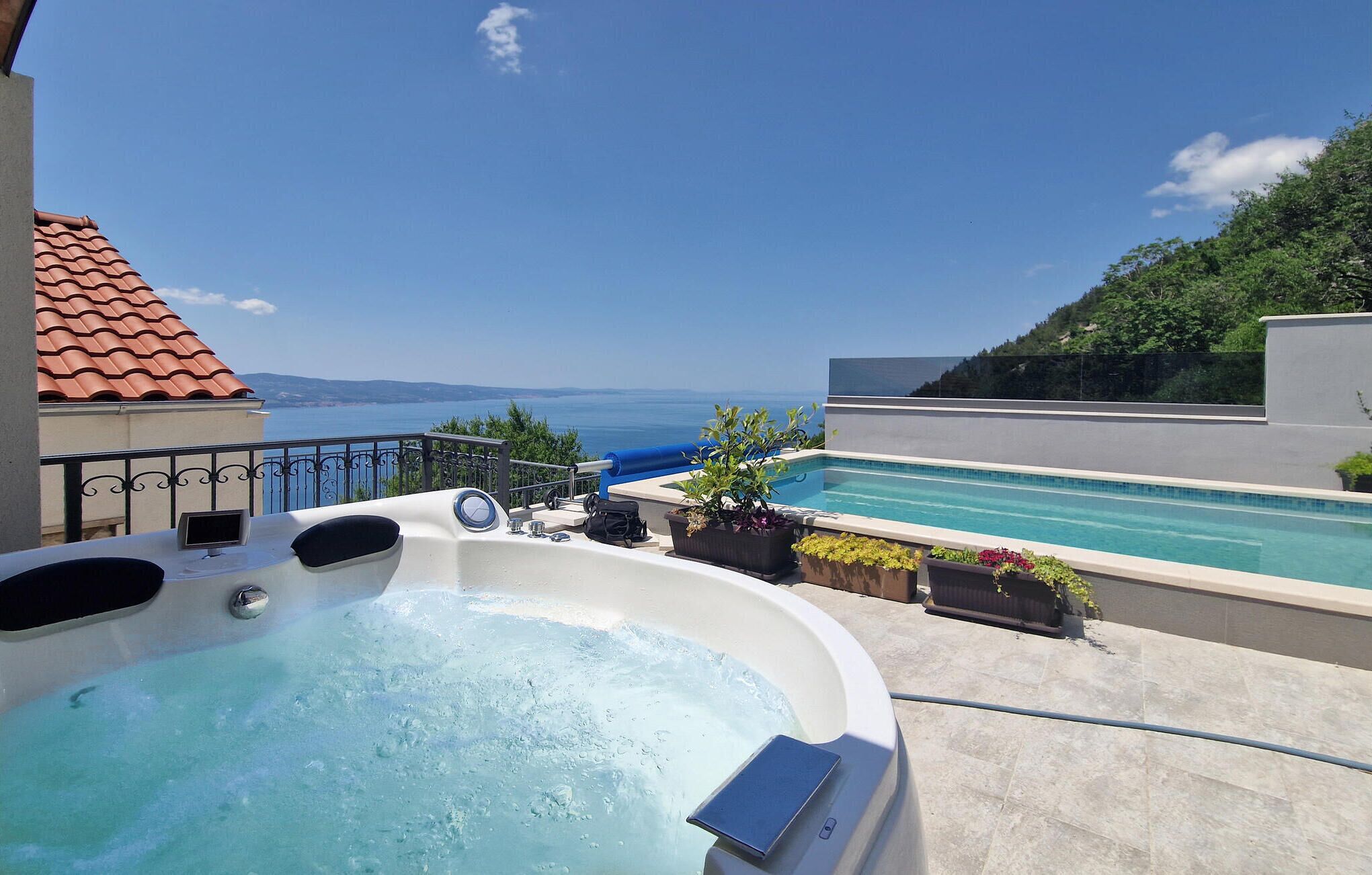 A hot tub with a view of the sea, a pool, and a terrace with potted plants.