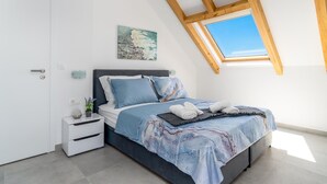 A bedroom with a skylight, a bed with a blue bedspread, a nightstand with a lamp, and a painting on the wall. - Pet friendly home in Stanici (Stanici)
