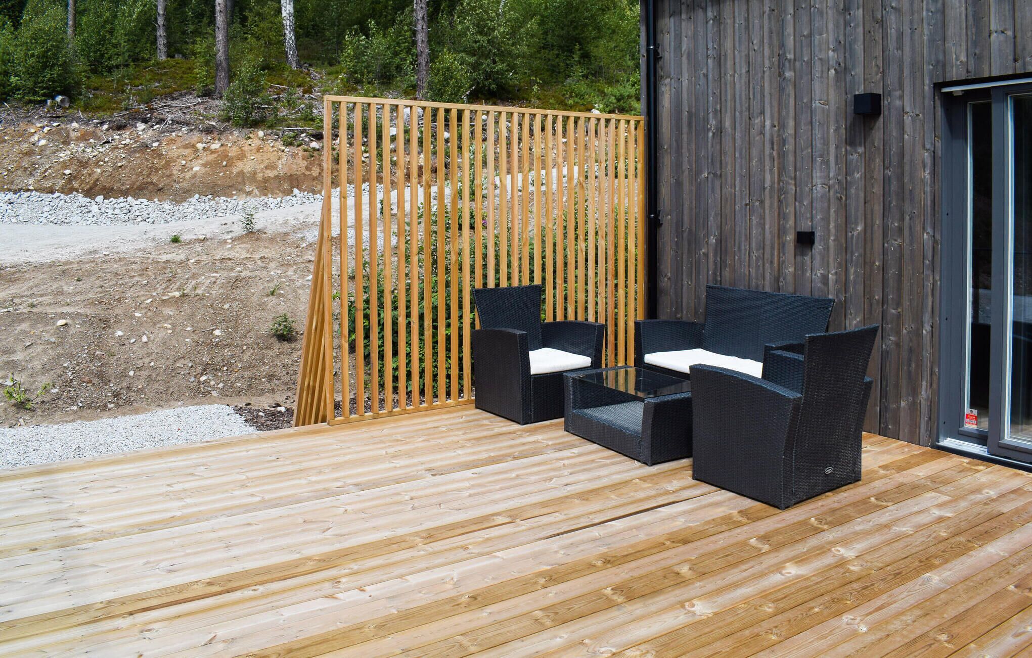 Een terras buiten met houten vloer en twee zwarte wicker stoelen met witte kussens.