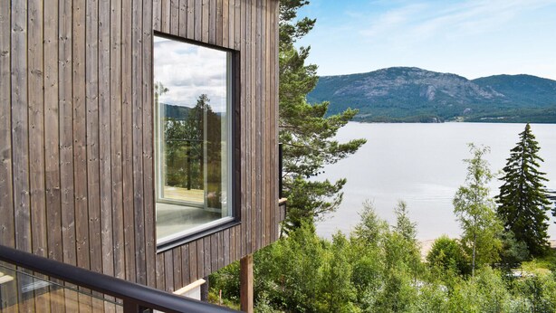 Una cabaña de madera con un amplio ventanal que da a un lago y montañas.