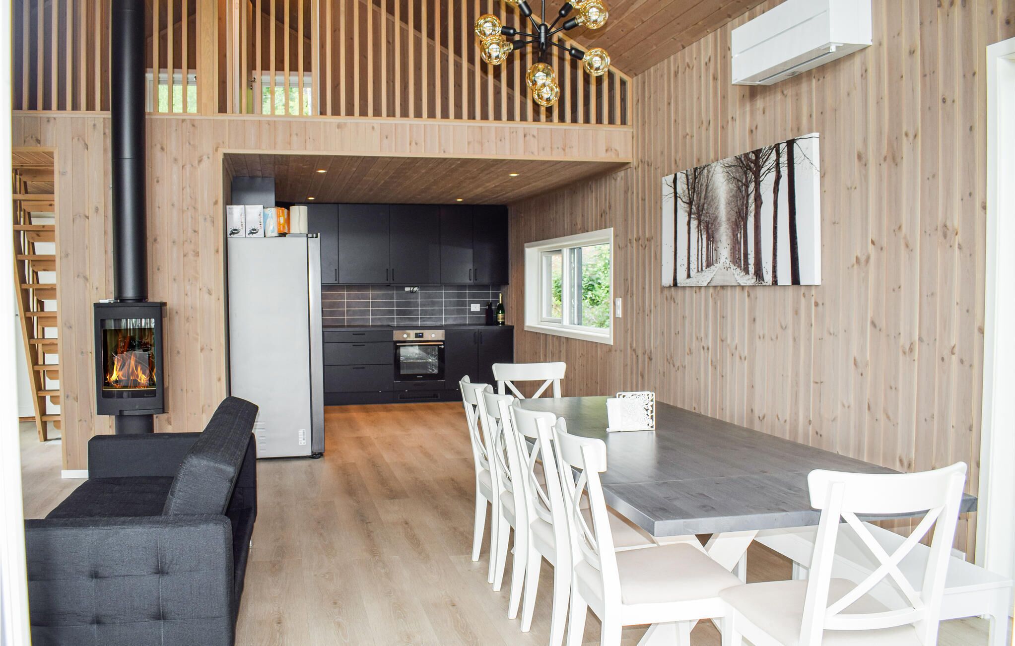 Een moderne keuken met donkere kastjes, een ingebouwde oven en een eethoek met een houten tafel en witte stoelen.