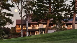 A modern two-story house with a large balcony, surrounded by trees and a grassy slope. - Ocean and golf course views! (Waikoloa Village)