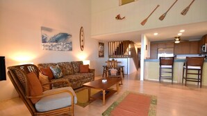 A spacious living area with a sofa, armchair, and coffee table. A kitchen is visible in the background with a microwave and chairs. - Ocean and golf course views! (Waikoloa Village)