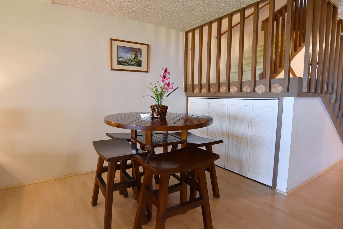 A dining area with a round wooden table and four chairs, a potted plant, and a staircase with wooden railings.