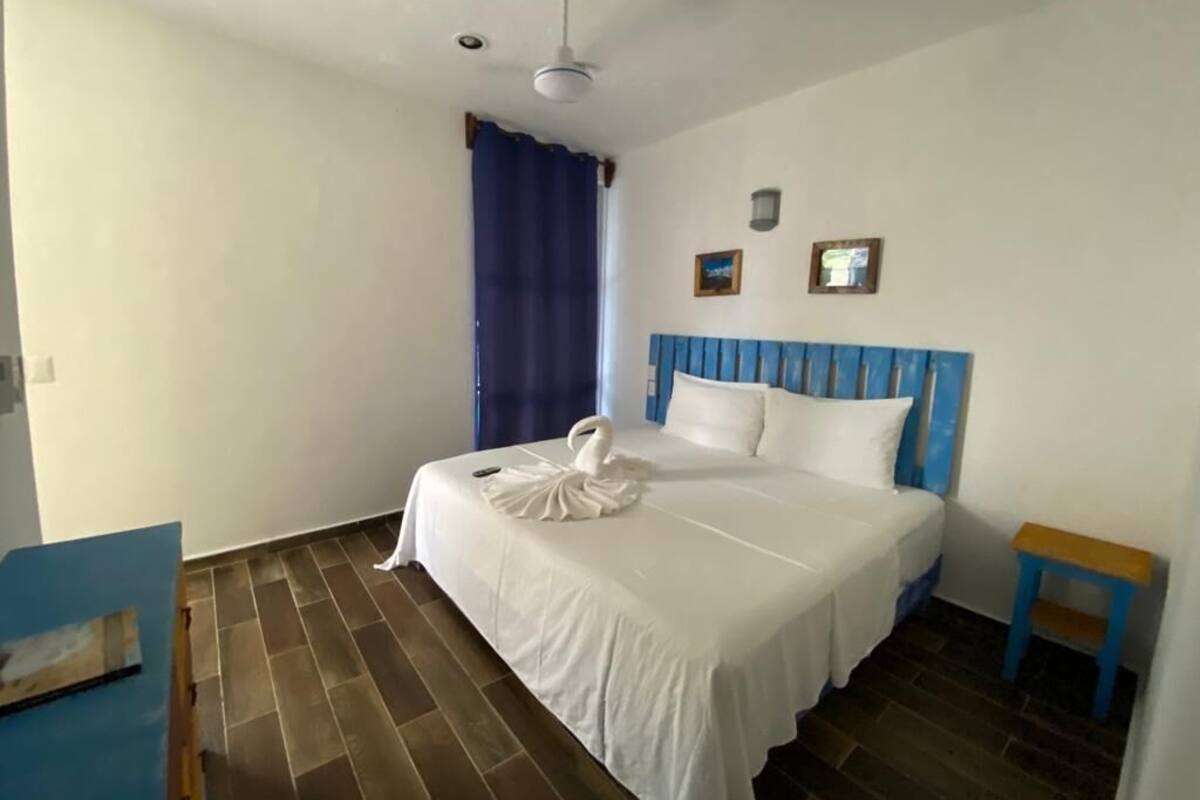 A hotel room with a bed, a blue headboard, a small table, and a ceiling fan.