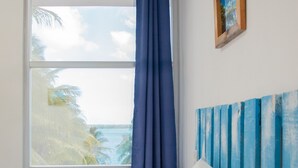 Un dormitorio con cama, vista al océano, ventana con cortinas azules y cabecera de madera.